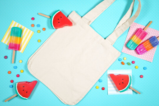 Summer beach vacation canvas tote bag flatlay styled with watermelon, candy and ice creams on a blue background. White product mock up with negative copy space for your text or design here.