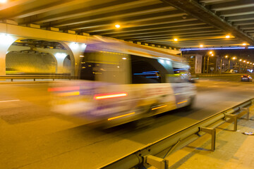 Fototapeta na wymiar The motion of a blurred minibus under the bridge in the evening.
