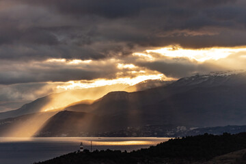 Southern coast of Crimea at sunset in winter. Sunset rays of the sun break through the clouds. Mountains, coast and beautiful scenery.