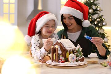 Mother and daughter decorating gingerbread house at table indoors