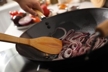 Man stirring onion slices in frying pan, closeup