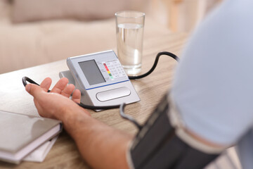 Man checking blood pressure at wooden table indoors, closeup