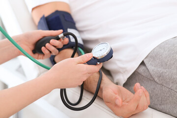 Doctor checking blood pressure of man in clinic, closeup