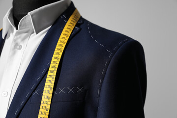 Semi-ready jacket with tailor's measuring tape on mannequin against grey background, closeup