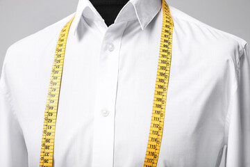 White shirt with tailor's measuring tape on mannequin against grey background, closeup