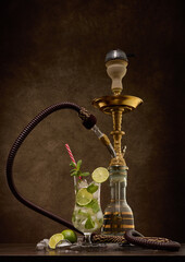 Hookah (shisha) and glass of Mojito cocktail with lime and ice on dark background. Weekend or holiday party