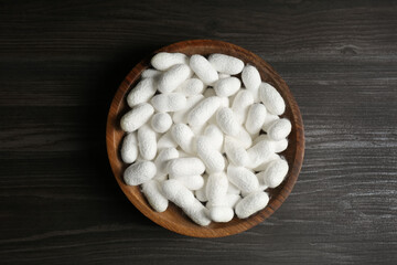 Fototapeta na wymiar White silk cocoons in bowl on wooden table, top view