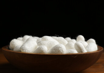 White silk cocoons in bowl on wooden table, closeup