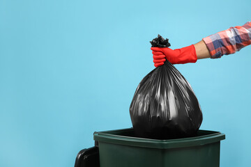 Man throwing garbage bag into bin on light blue background, closeup. Space for text