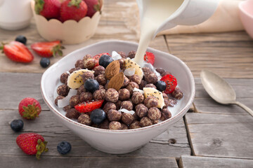 Milk falling into cereal bowl with fruits on wooden table