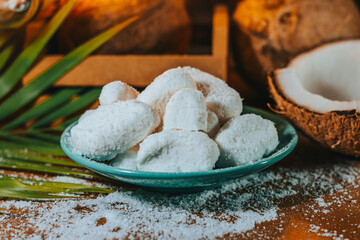 Concept of coconut candy with a ripe half cut coconut with green leaves on a brick wall background