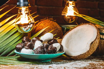 Concept of coconut candy with a ripe half cut coconut with green leaves on a brick wall background