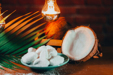 Concept of coconut candy with a ripe half cut coconut with green leaves on a brick wall background