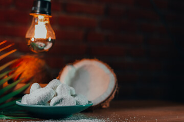 Concept of coconut candy with a ripe half cut coconut with green leaves on a brick wall background