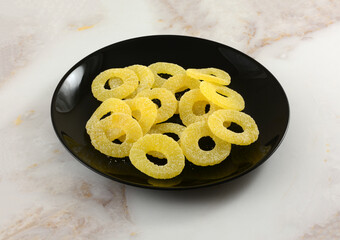 Sour pineapple ring gummy candy on black snack plate on table
