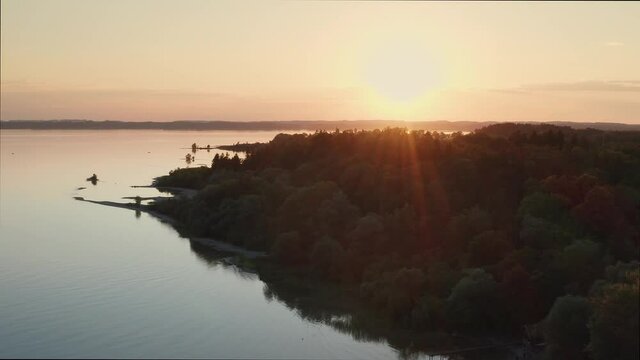 Lake Chiemsee in Bavaria with the Alp mountains during sunset from above, coast near village Chieming, during summer, flying forwards
