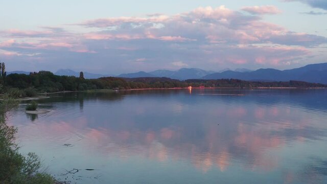 Lake Chiemsee in Bavaria with the Alp mountains during sunset from above, coast near village Chieming, during summer, flying forwards
