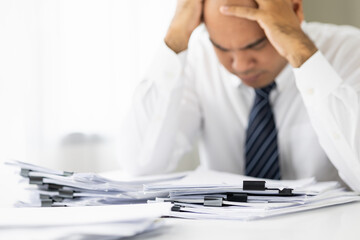 A young business man stressed managing paperwork in the office. Many paperwork that is not finished. Documents in the company about finance and information of the company.