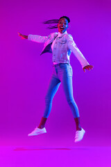 Fototapeta na wymiar Trendy stylish energetic young African American woman jumping in futuristic purple cyberpunk neon light background