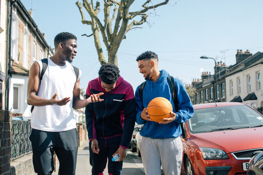 Group of three male friends with basketball walking down road and laughing