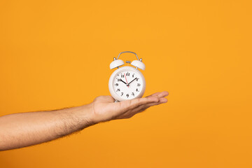 Close up male hand holding alarm clock on isolated yellow background.