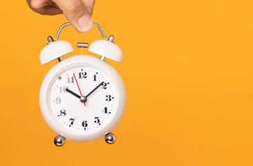 Close up male hand holding alarm clock on isolated yellow background.