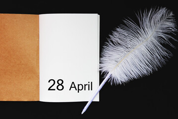 Day 28 of April month, empty notebook and white quill pen. Empty space for text. 