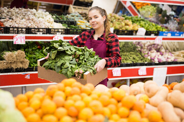 Cheerful european woman seller offering for sale fresh spinach at grocery store