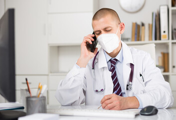 Positive professional doctor man in protective mask enters patient data into database at his workplace in hospital