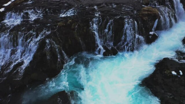 Breathtaking aerial tilt up pf crashing waterfalls and snowy mountains in backdrop. Iceland Trip