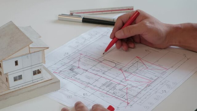 An Asian (Thai) architect is writing a comment  on the Thai house  construction plan by a red pen. In order for the staff to improve.