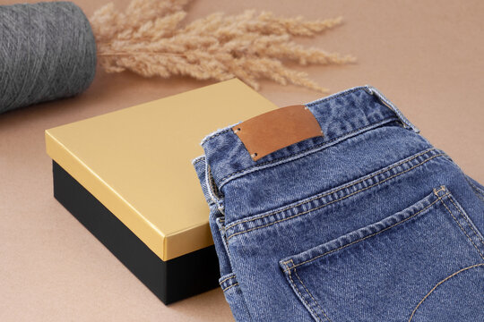 close-up leather empty tag or label on the back pocket of blue jeans on a vase of spool yarn with dry pampas grass and black golden box.