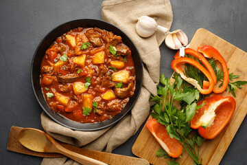 Goulash, beef stew with vegetables in tomato sauce. Top view. Dark (black) background.