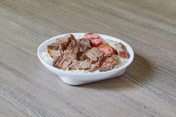 Marmitex with white rice, beans and barbecue on a textured wooden table.