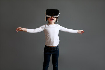 Fascinated female child in white long sleeve shirt wearing virtual reality glasses over grey background