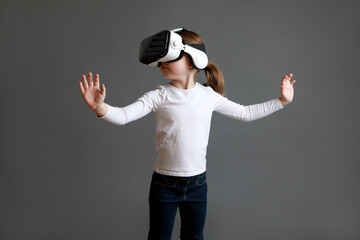 Fascinated female child wearing virtual reality glasses over grey background