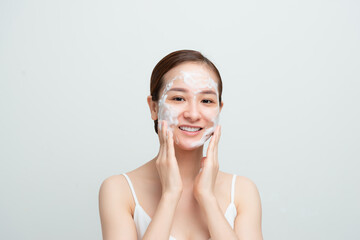 Close-up of happy smiling asian woman using daily-care skin cleansing foam and looking delighted, white background