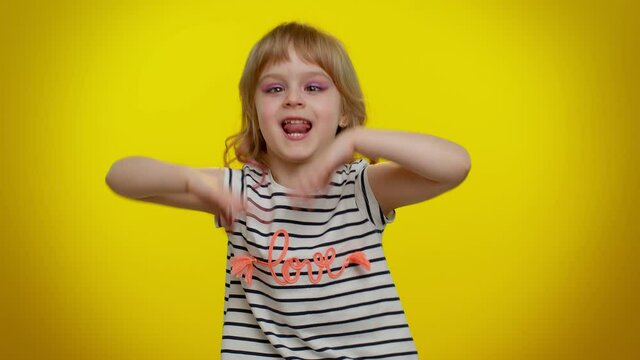 Playful funny little blonde kid child 5-6 years old demonstrating tongue out, fooling around, making silly faces, madness. Little bit crazy teenager children girl emotions on yellow studio background