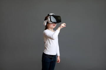 Little preschool girl experiencing virtual reality eyeglassses in white long sleeve shirt over grey background