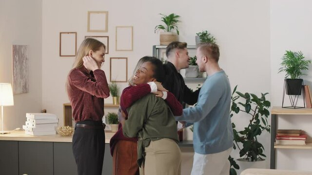 Slowmo medium shot of happy young people visiting their friends in cozy apartment. They are chatting and hugging