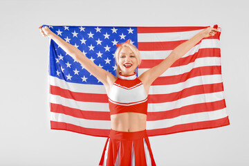 Beautiful cheerleader with USA flag on light background