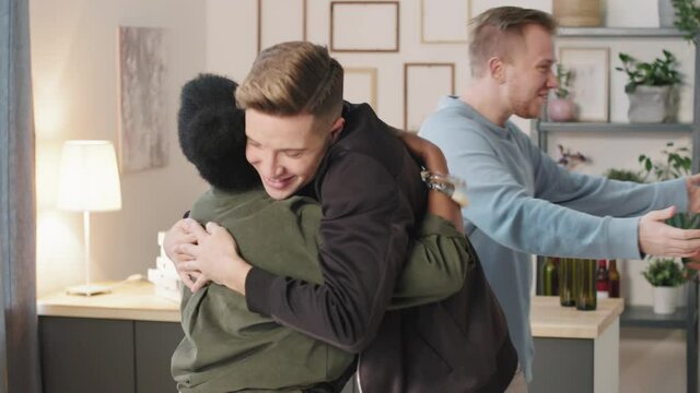Slowmo of happy young men and women smiling and hugging each other in cozy apartment