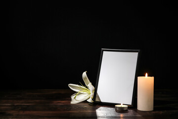 Photo frame with lily flower and candles on table against dark background