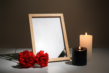 Photo frame with carnation flowers and candles on table against dark background