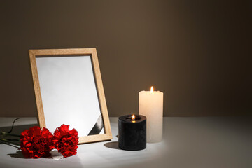 Photo frame with carnation flowers and candles on table against dark background