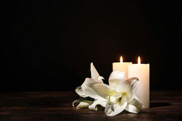 Candles with lily flowers on table against dark background