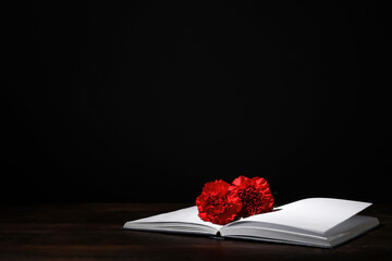 Book with carnation flowers on table against dark background