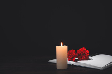 Book with carnation flowers and candle on table against dark background