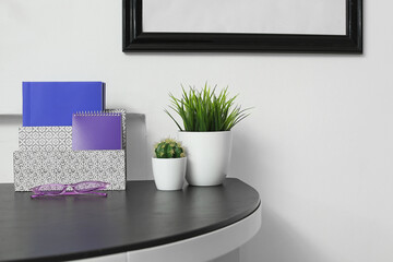 Modern organizer and houseplants on table near white wall