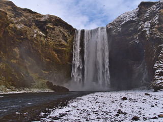 Beautiful front view of stunning waterfall Skógafoss (height 60m), a popular tourist destination on the south coast of Iceland near ring road, in winter season with snow and rugged rocks.